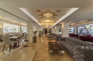 Een ruime hotellobby met een hoge plafond, gedetailleerde kroonluchters, comfortabele zitplaatsen en grote ramen met uitzicht op het omliggende landschap.