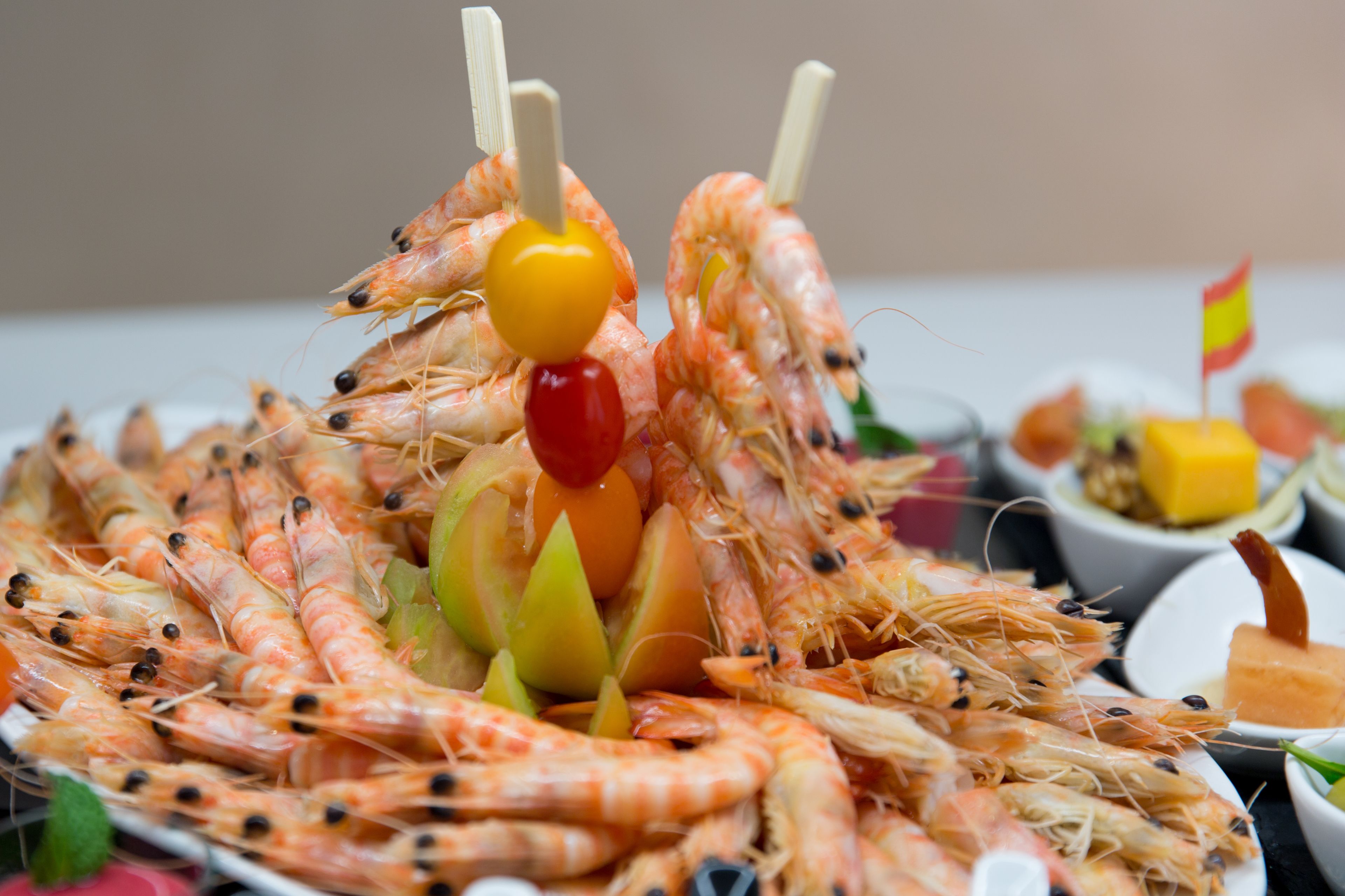 A platter of grilled shrimp with toothpicks and a small flag, surrounded by various side dishes.