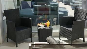 A modern outdoor seating area with wicker chairs and a glass table, featuring a breakfast setup with a beverage and pastries.