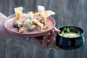 Een persoon houdt een bord met dumplings en een kom soep vast.