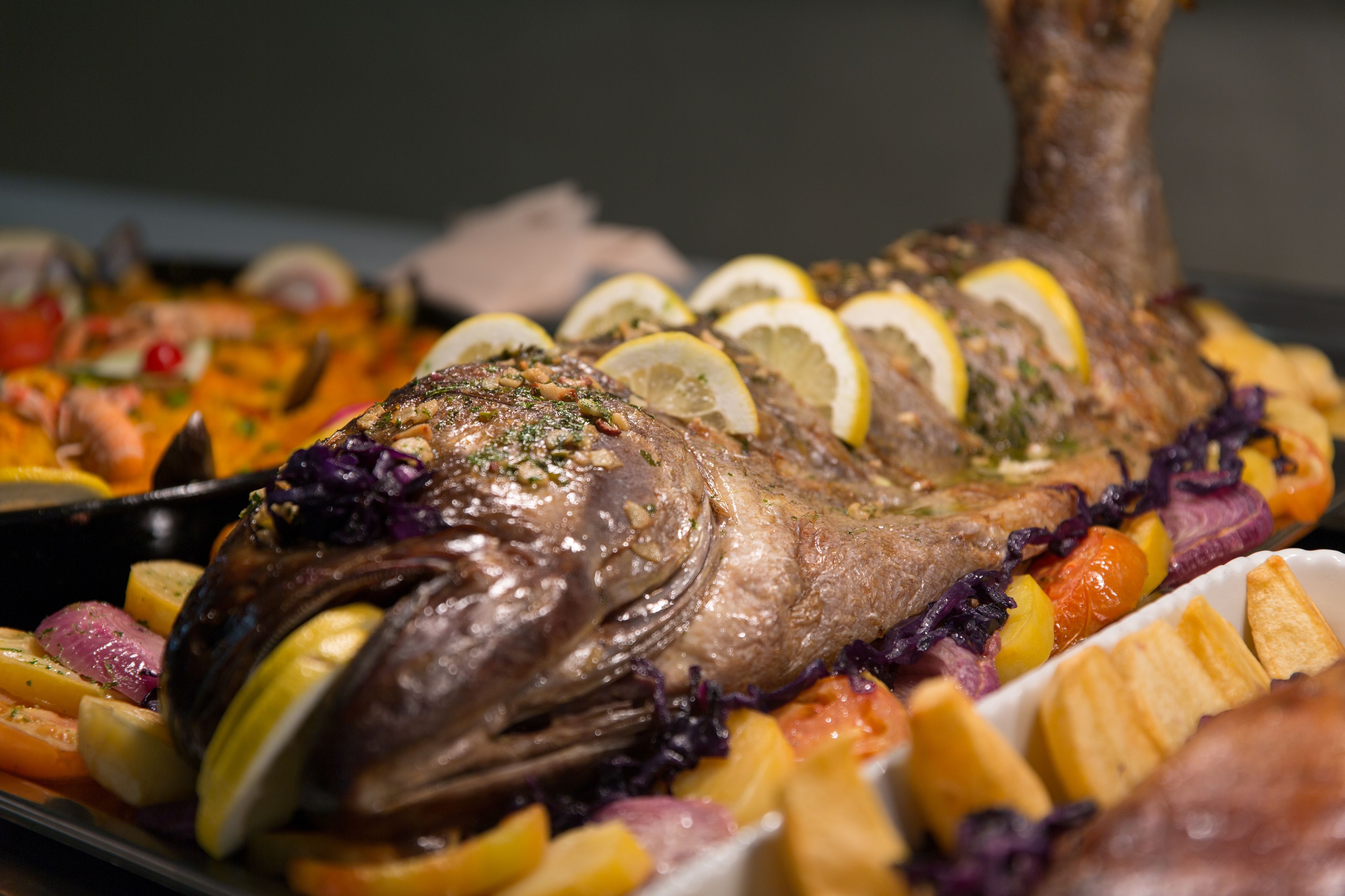 Pescado entero asado con rodajas de limón y verduras en una bandeja.
