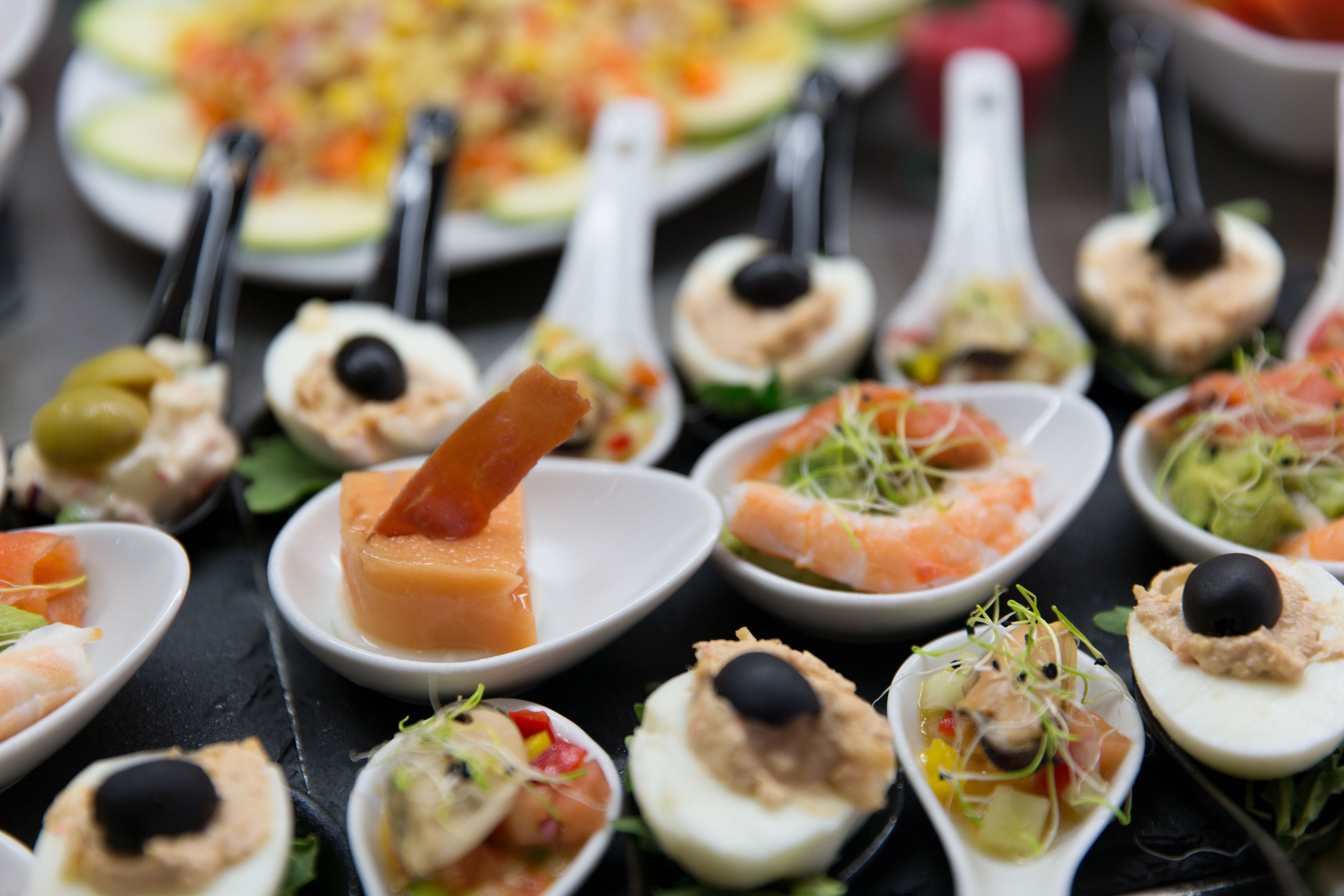 A variety of appetizers arranged on white plates with black spoons.