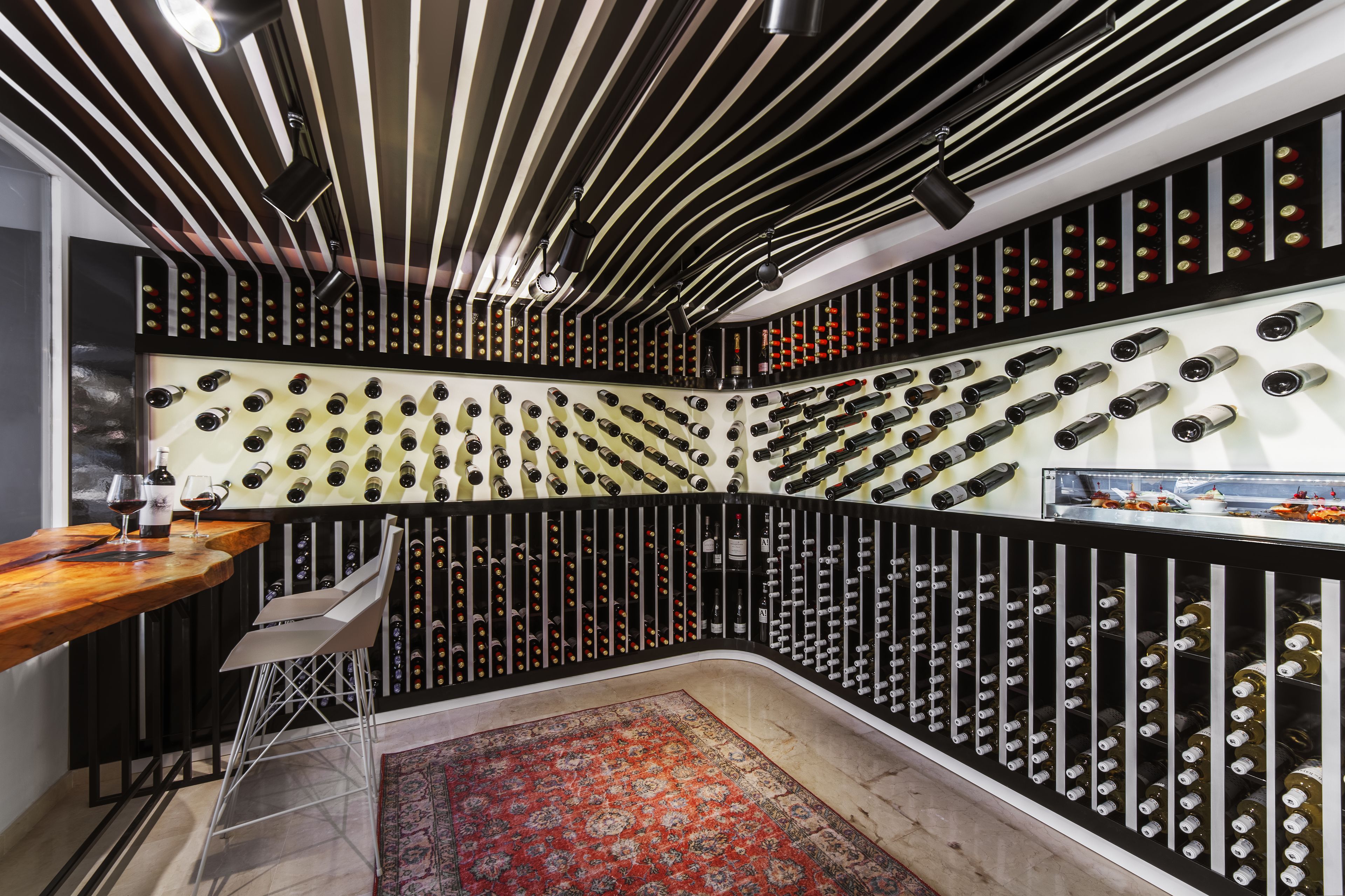A wine cellar with rows of wine bottles, a wooden bar, and a red patterned rug.