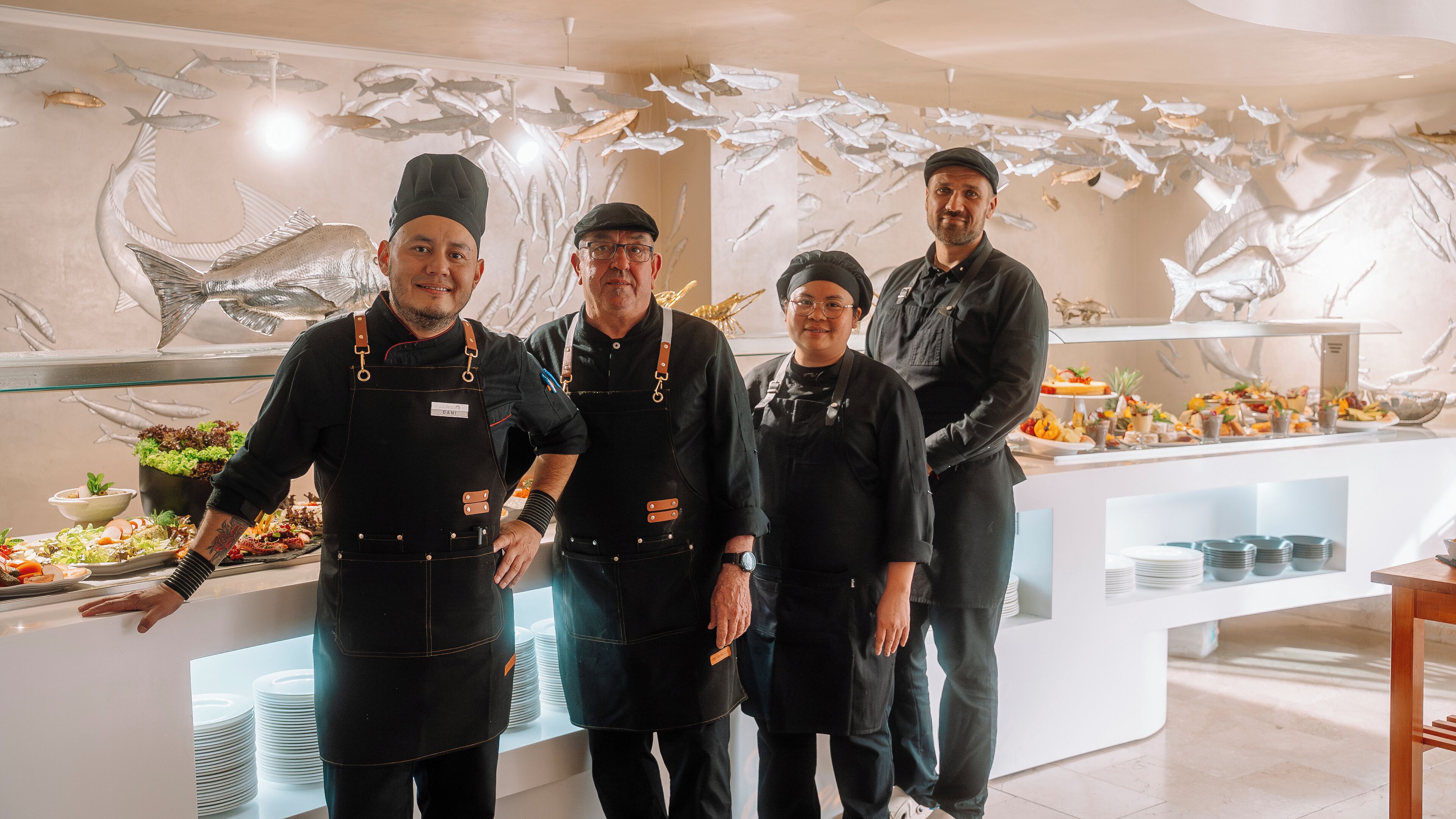 A group of four chefs in a modern kitchen with a seafood-themed wall art.