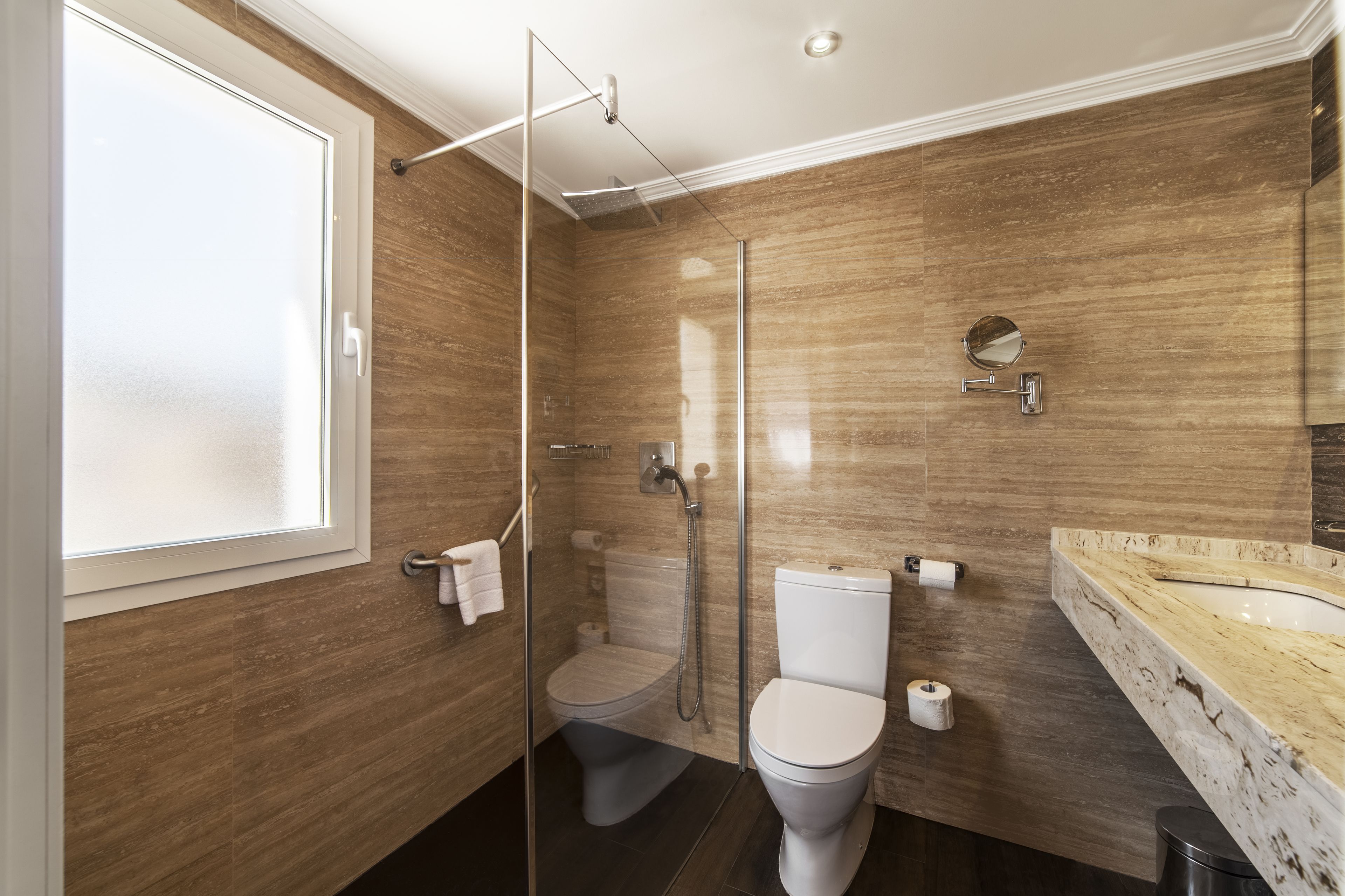 Une salle de bain moderne dotée d’une douche à parois de verre, de toilettes et d’un lavabo en marbre.