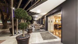A modern outdoor area with seating, potted plants, and a glass storefront. - Essence Hotel Boutique (Torremolinos)
