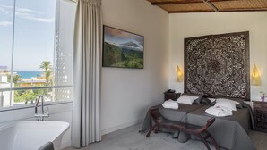 A hotel room with a large window, a bathtub, two beds, a decorative headboard, and a nightstand with a lamp. - Essence Hotel Boutique (Torremolinos)