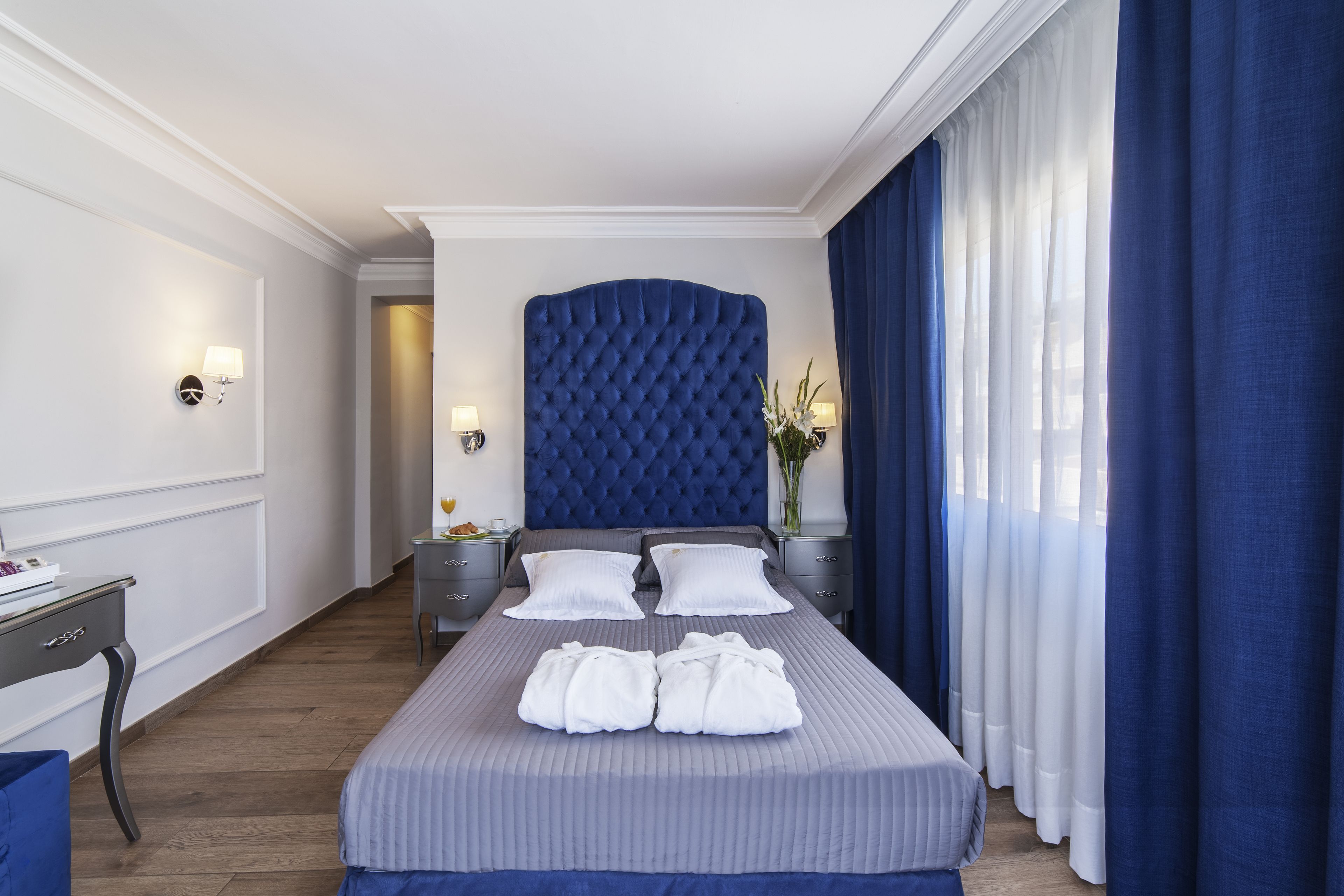 Habitación de hotel con una cama grande, una mesita de noche, un escritorio y una ventana con cortinas.