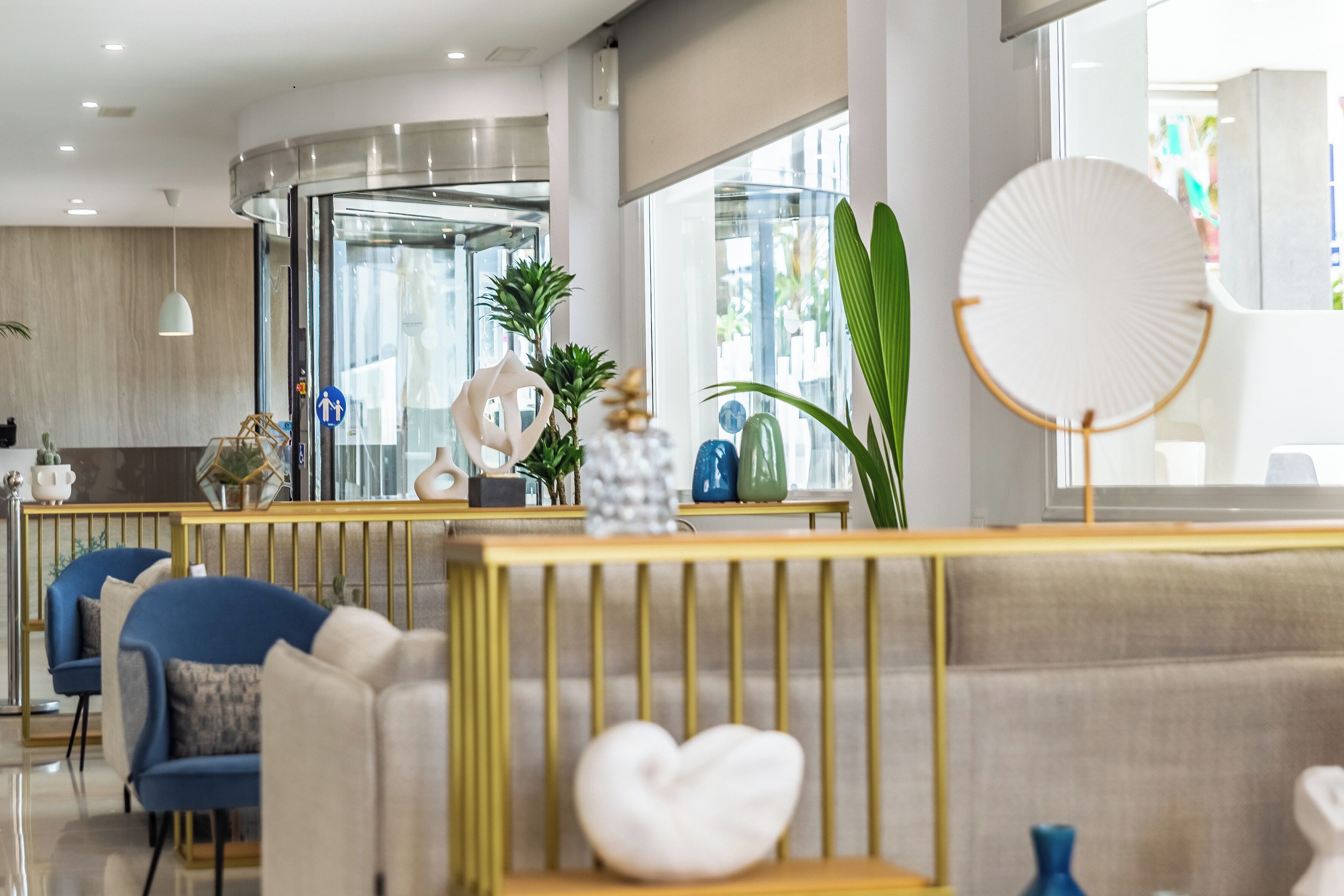 A modern hotel lobby with a seating area, a reception desk, and a large window providing a view of the outside.