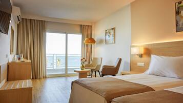 A hotel room with a bed, two chairs, a desk, a TV, and a view of the sea.