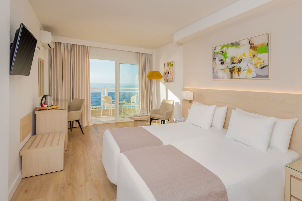 A hotel room with a large bed, a desk, a chair, and a view of the ocean.