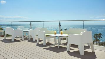 Une terrasse dotée de meubles blancs et d’une table, offrant une vue sur une étendue d’eau.