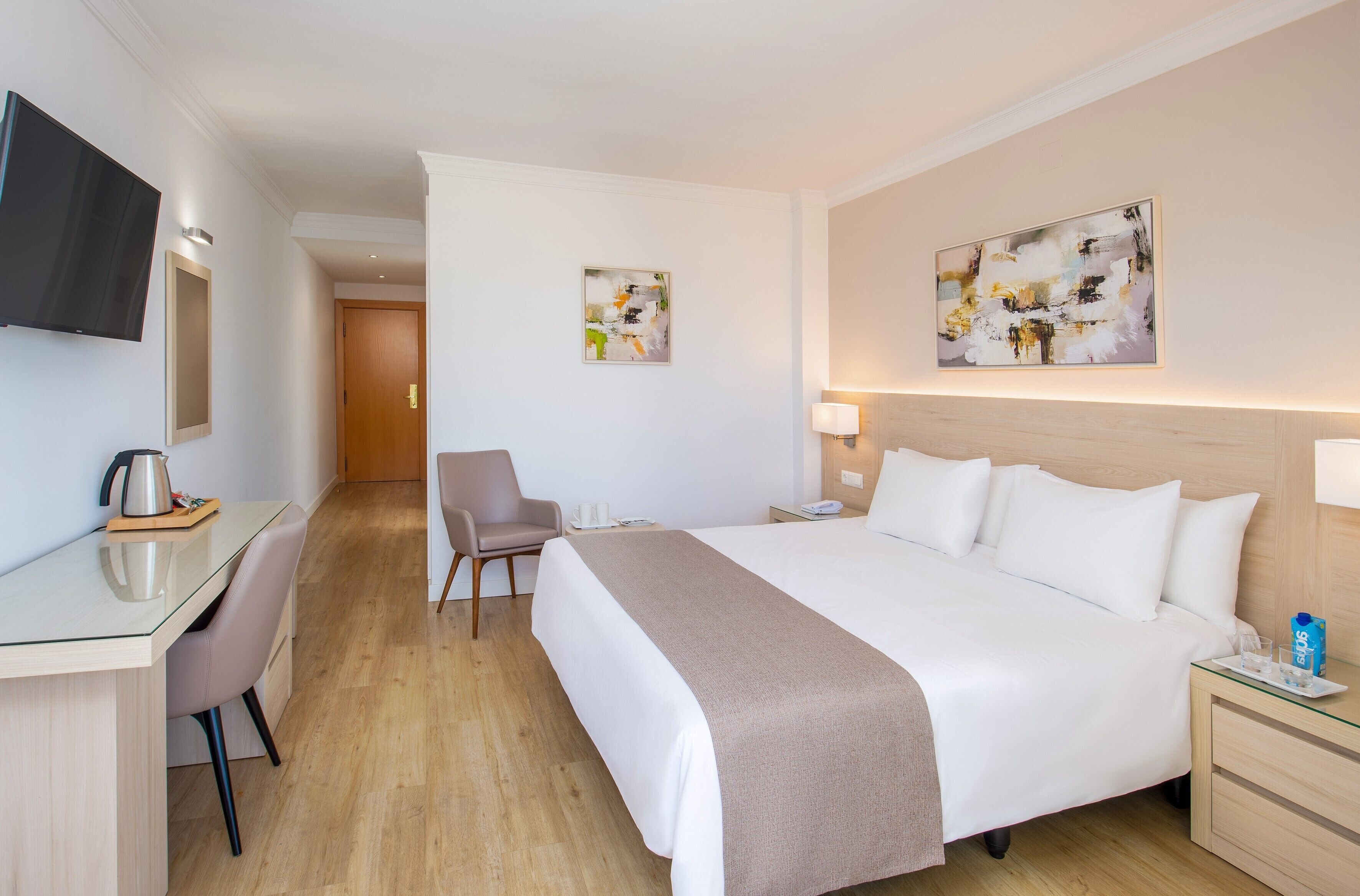 Een hotelkamer met een bed, nachtkastje, stoel, bureau en een televisie.