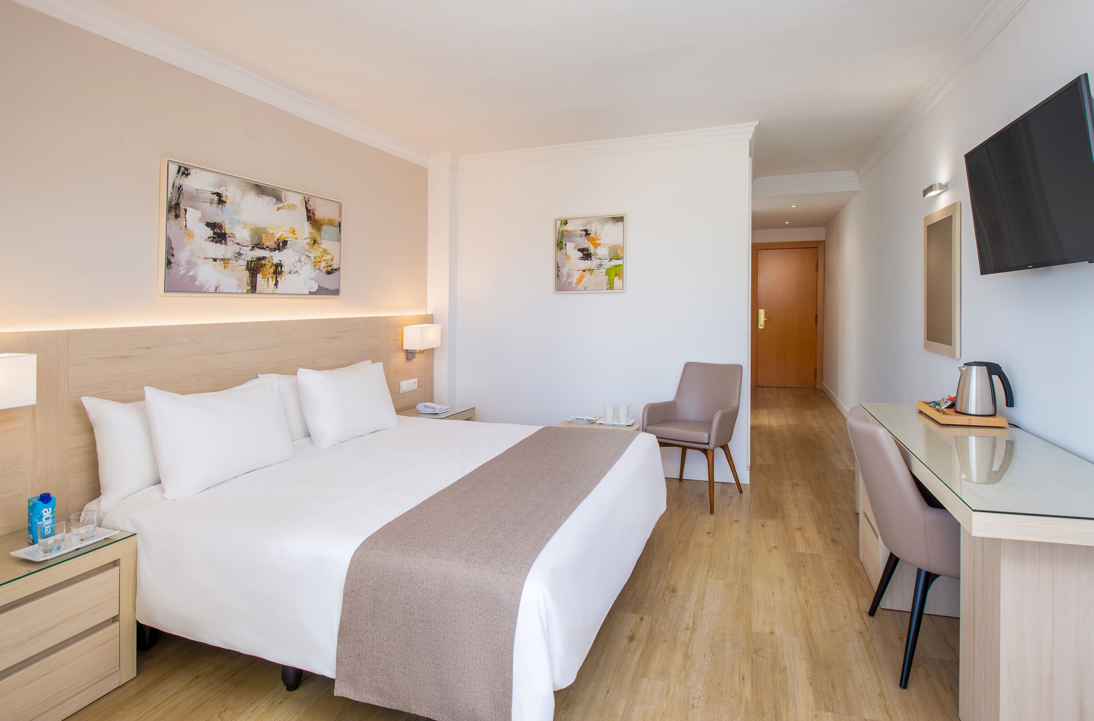 A hotel room with a large bed, bedside tables, a desk, and a TV.