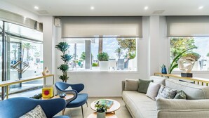 A modern living room with a sofa, two armchairs, a coffee table, and large windows with a view of palm trees and buildings. - Hotel Las Arenas, Affiliated by Meliá (Benalmádena)
