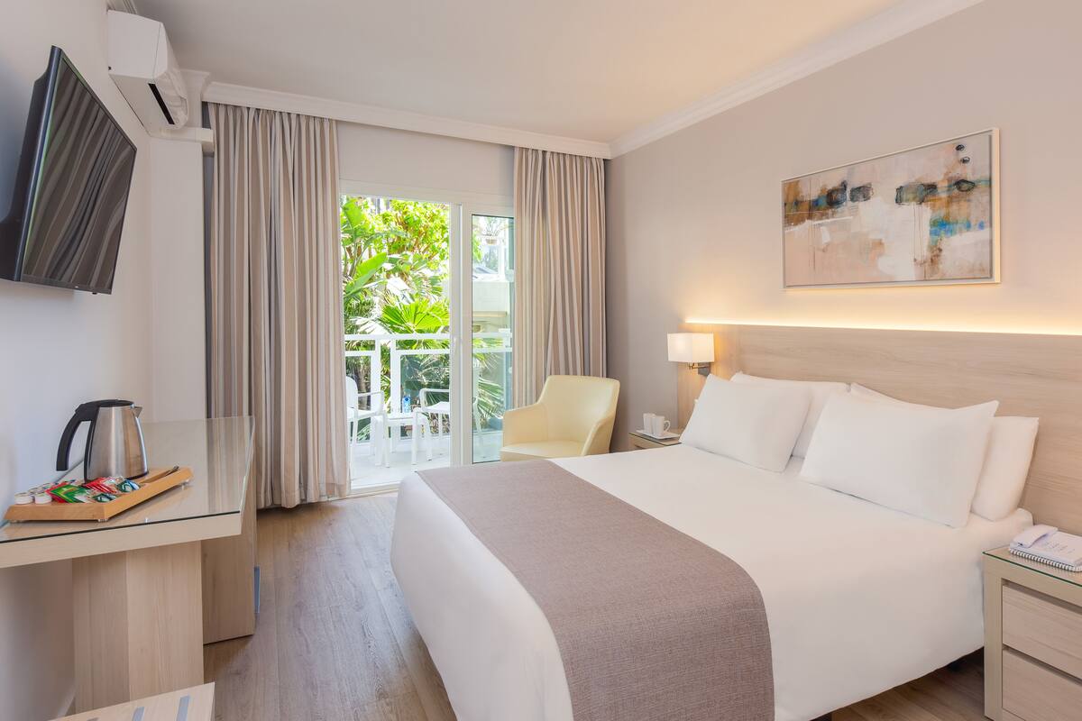 A hotel room with a bed, a desk, a chair, a TV, and a painting on the wall.