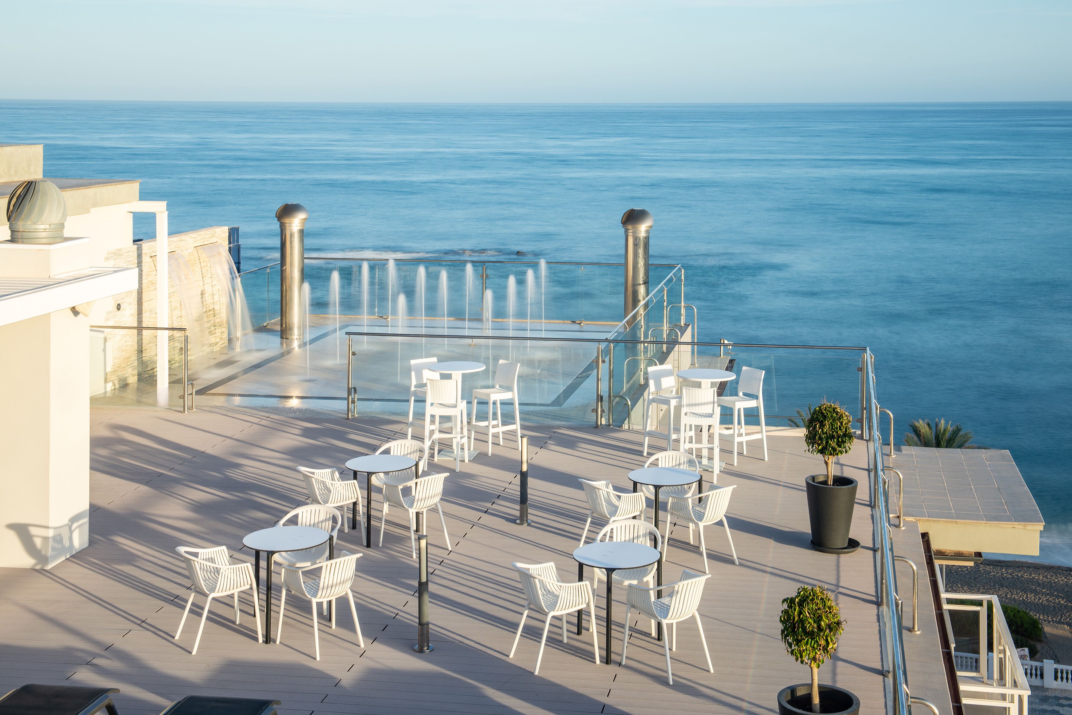 Terraço no telhado com cadeiras e mesas brancas, vista para o mar.