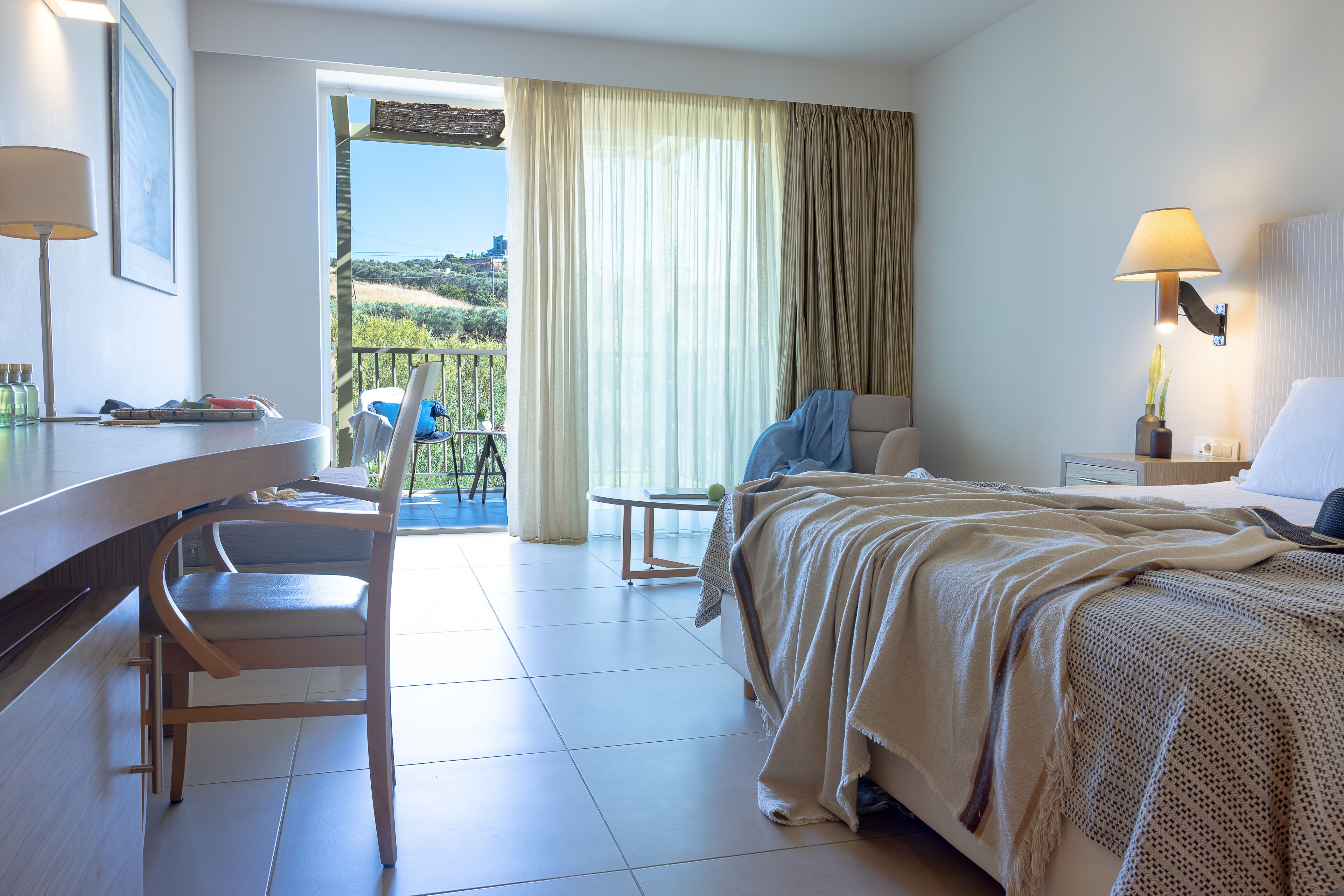 Une chambre d’hôtel équipée d’un lit, d’un bureau, d’une chaise, d’une petite table et offrant une vue sur l’extérieur.