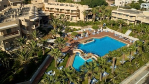 Een resort met een centraal gelegen zwembad, omringd door ligbedden en palmbomen.