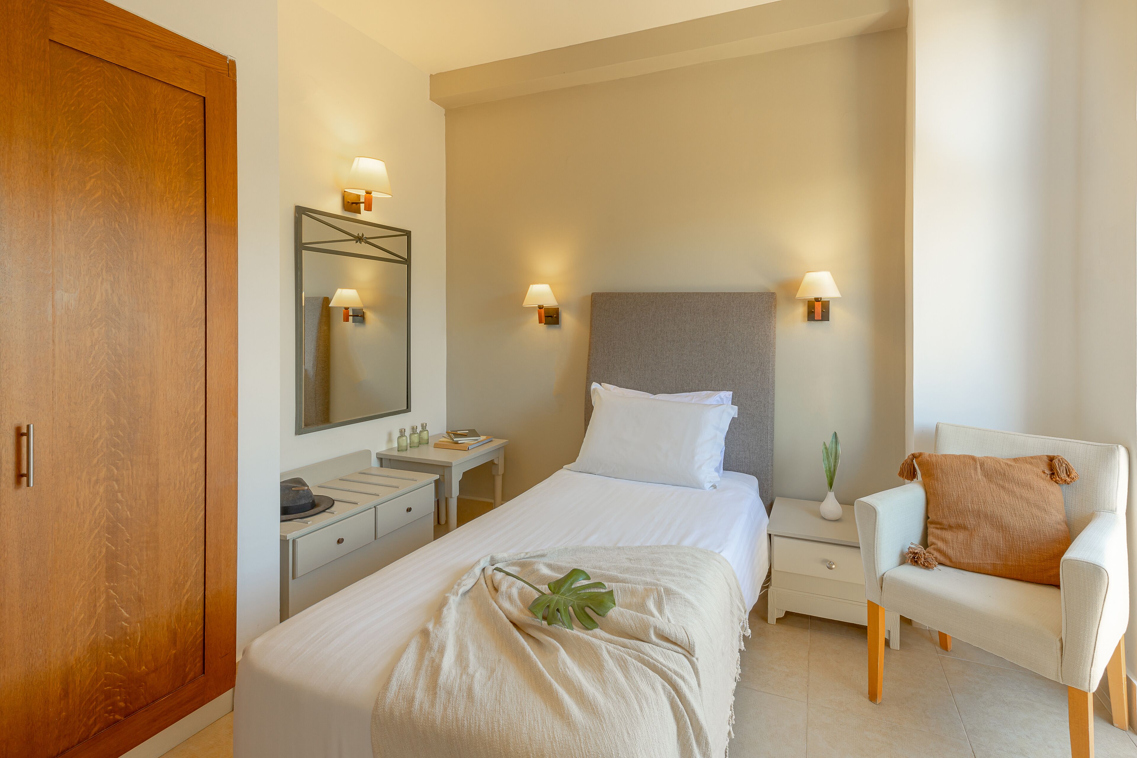 A hotel room with a bed, bedside table, chair, and a wooden wardrobe.