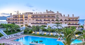 Un hôtel à plusieurs étages doté d’une piscine, de chaises longues extérieures et offrant une vue sur la mer.