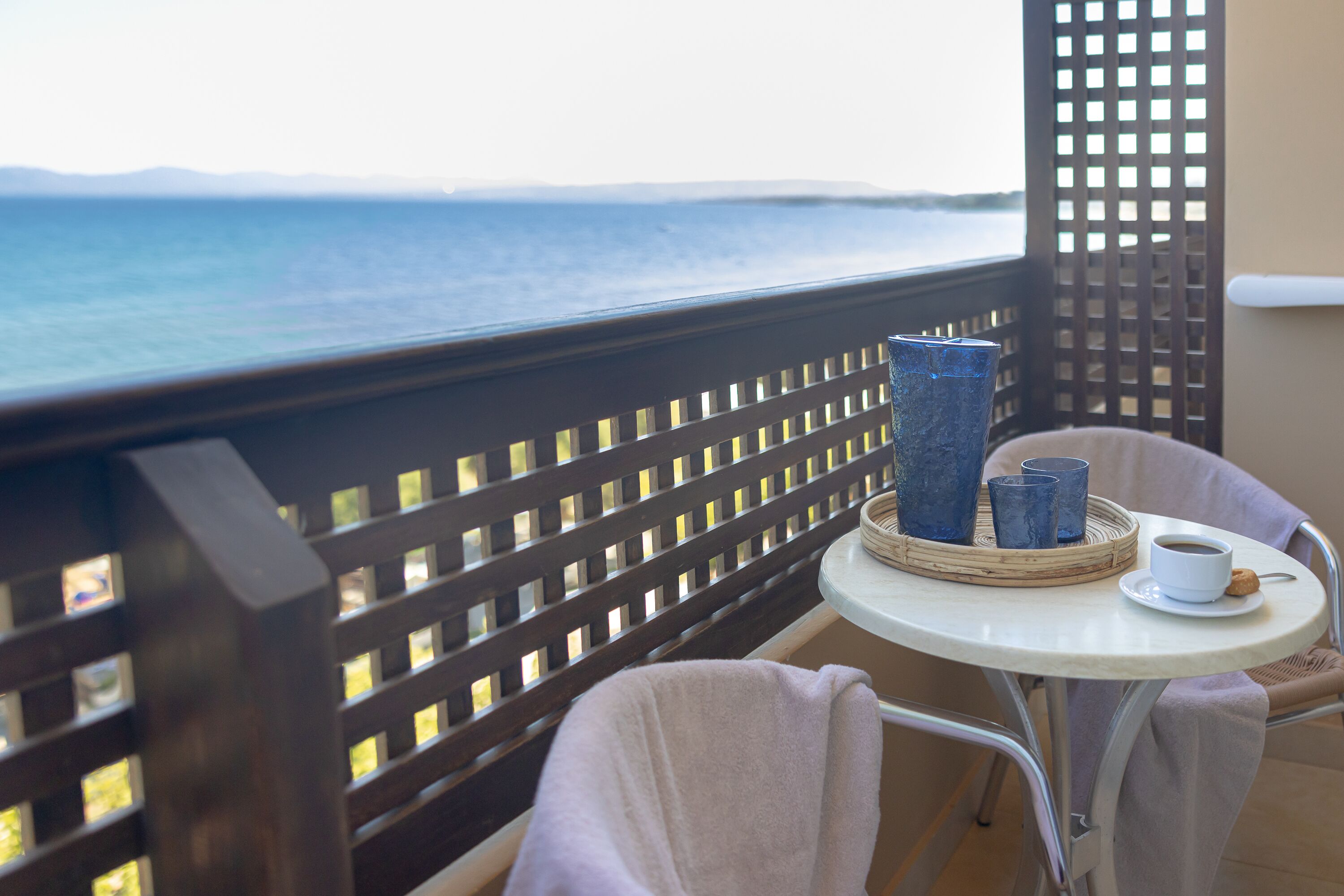 Un balcon donnant sur la mer, une table avec une tasse et une soucoupe, et deux vases bleus.