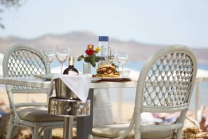 Une table dressée pour deux personnes, avec une bouteille de gin, des verres, une assiette de nourriture et un vase avec une fleur.