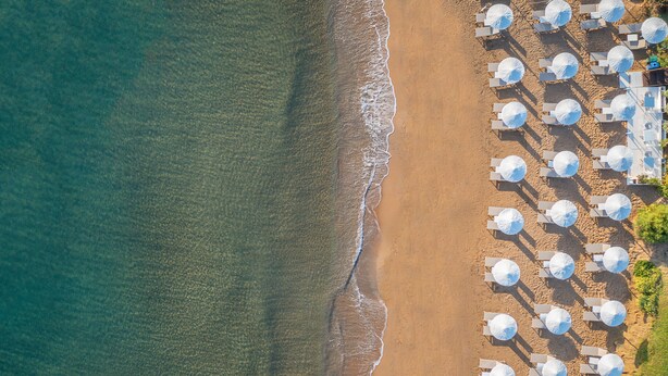Luchtbeeld van een strand met rijen witte parasols en ligstoelen, wat een resort aan het strand doet vermoeden.
