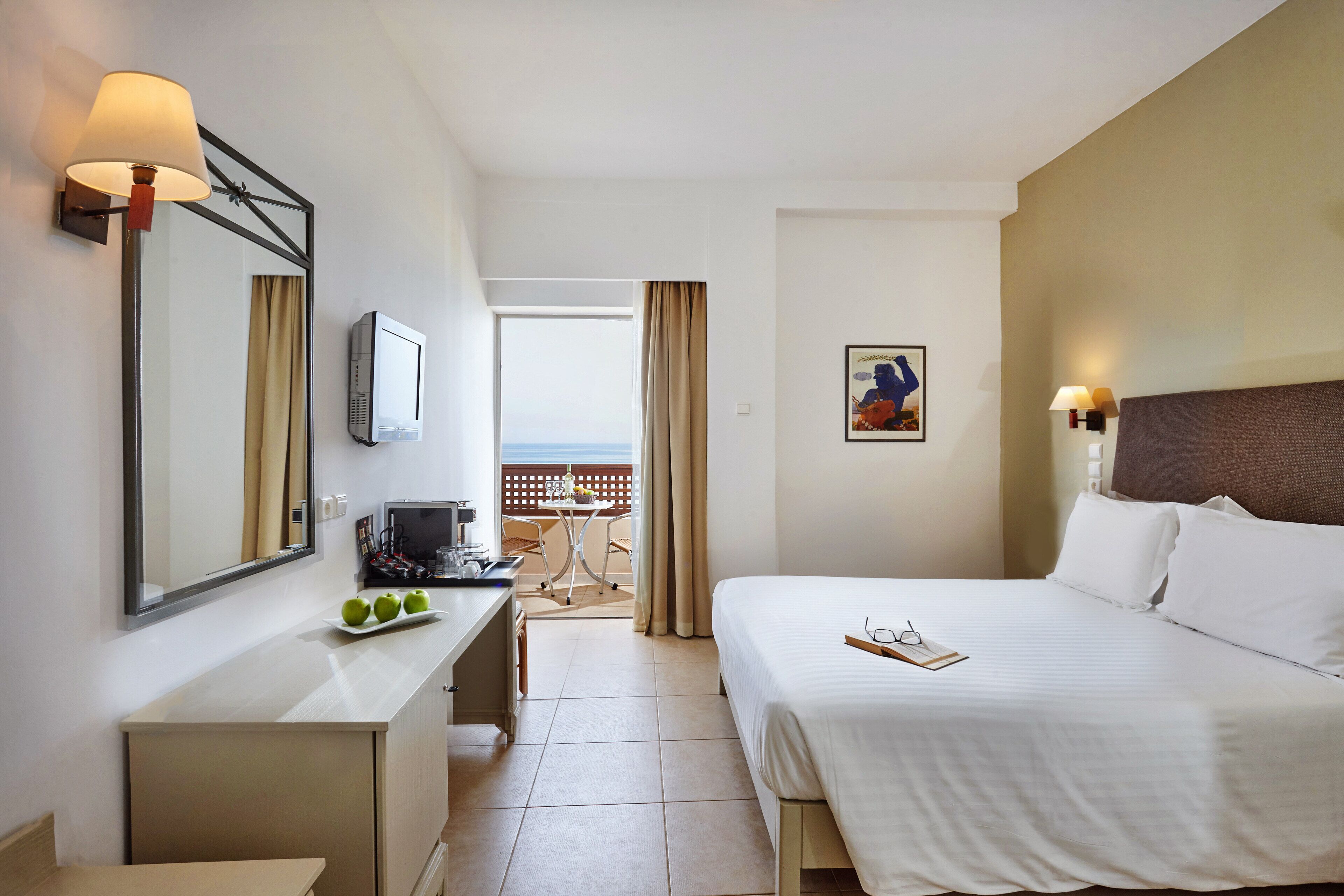 A hotel room with a bed, desk, and a view of the sea.
