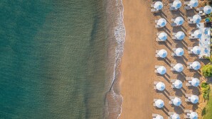 Luchtbeeld van een strand met rijen witte parasols en ligstoelen, wat een resort aan het strand doet vermoeden.