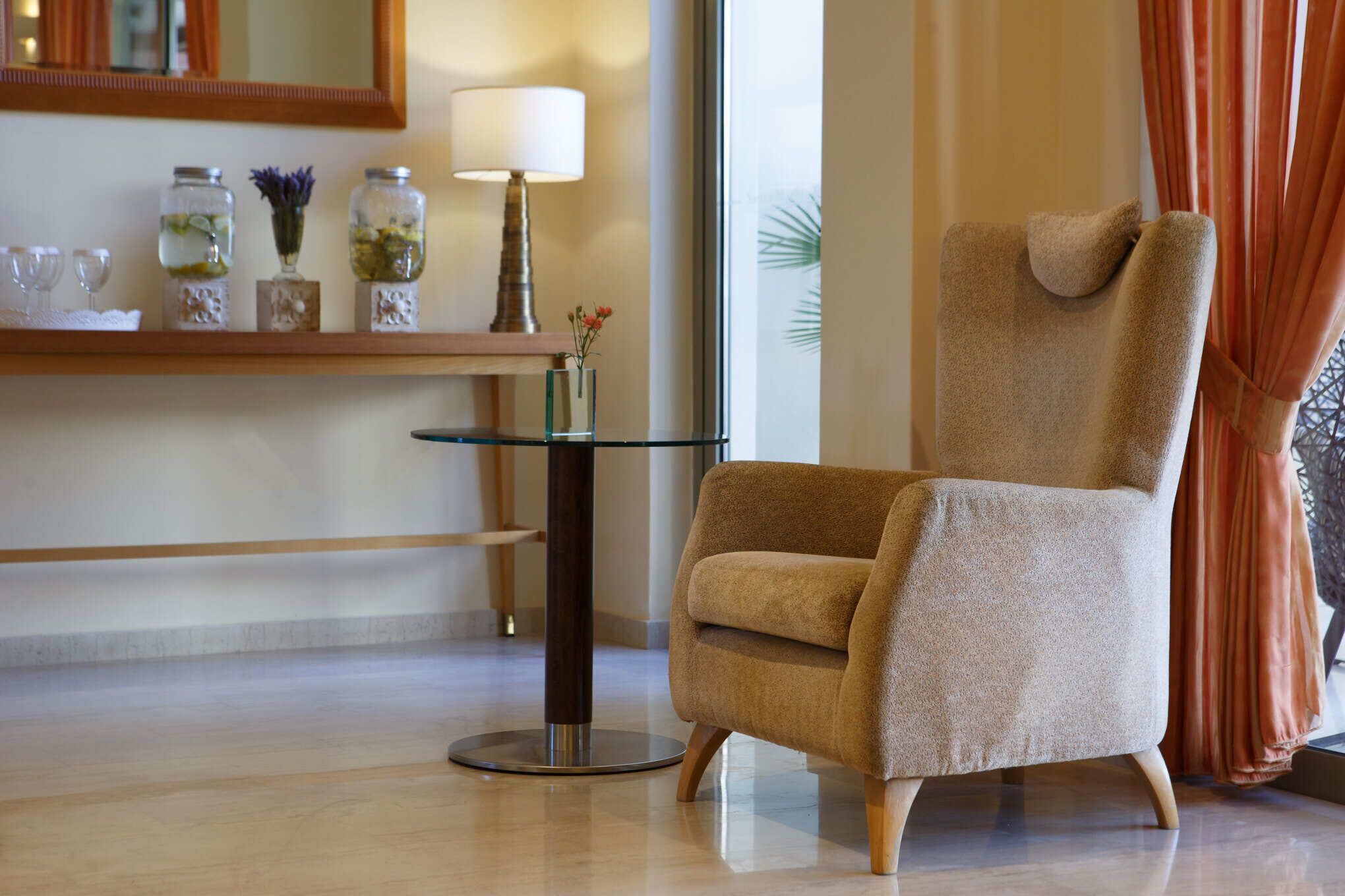 A modern room with a beige armchair, a glass table, and decorative jars on a wooden shelf.
