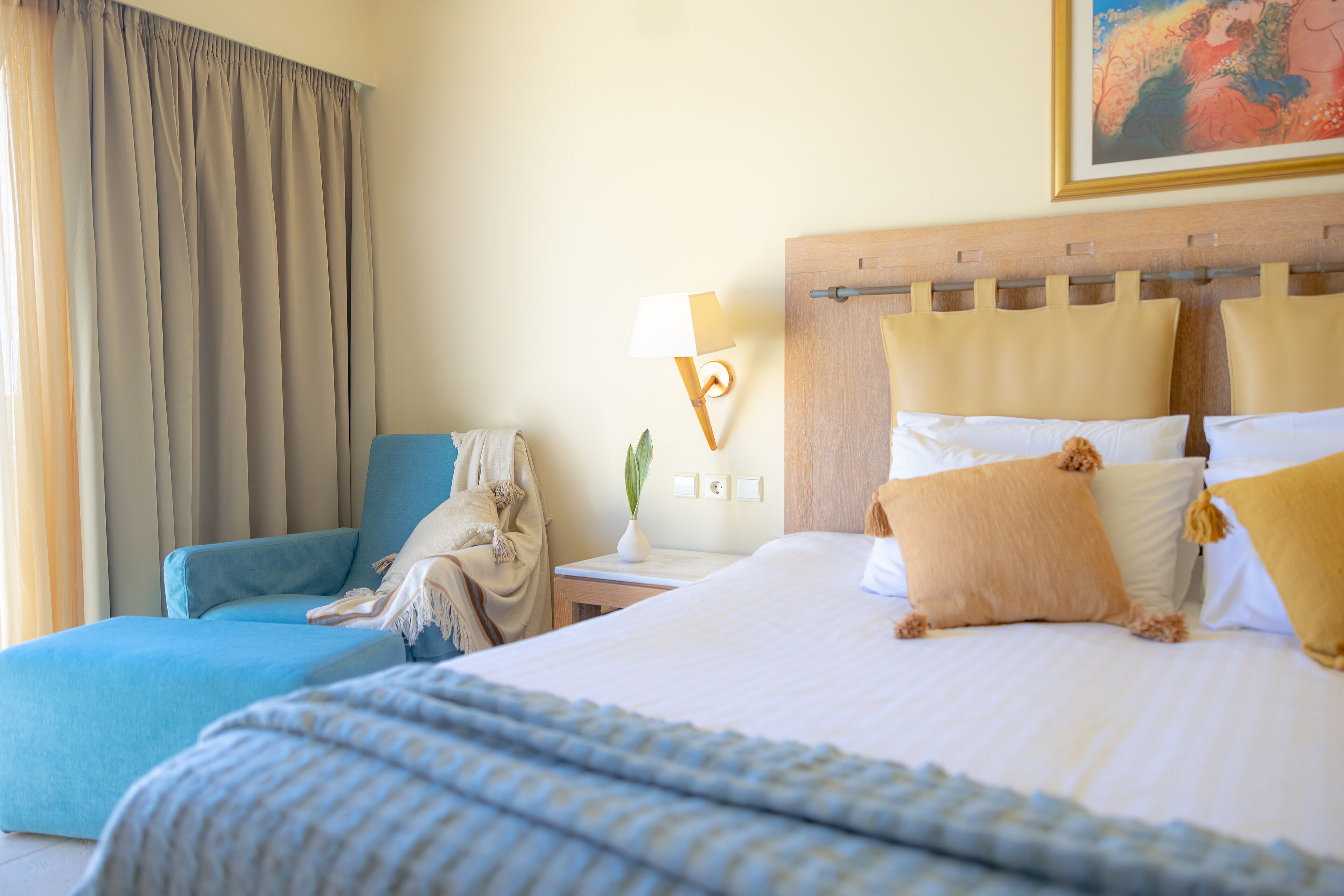 Een hotelkamer met een bed, een blauwe fauteuil, een nachtkastje met een lamp en een schilderij aan de muur.