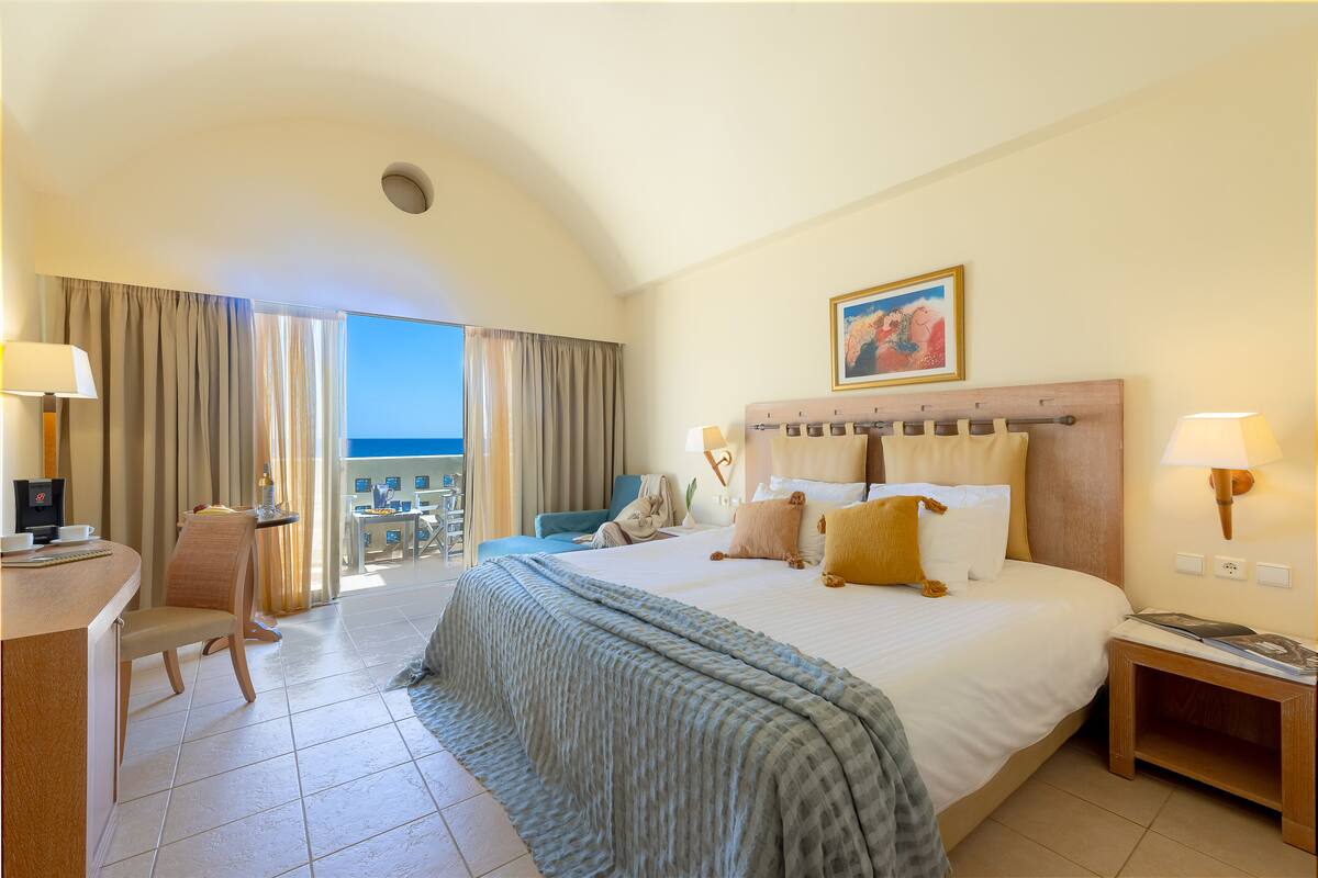 Habitación de hotel con cama, escritorio, silla, lámpara y vistas al exterior.
