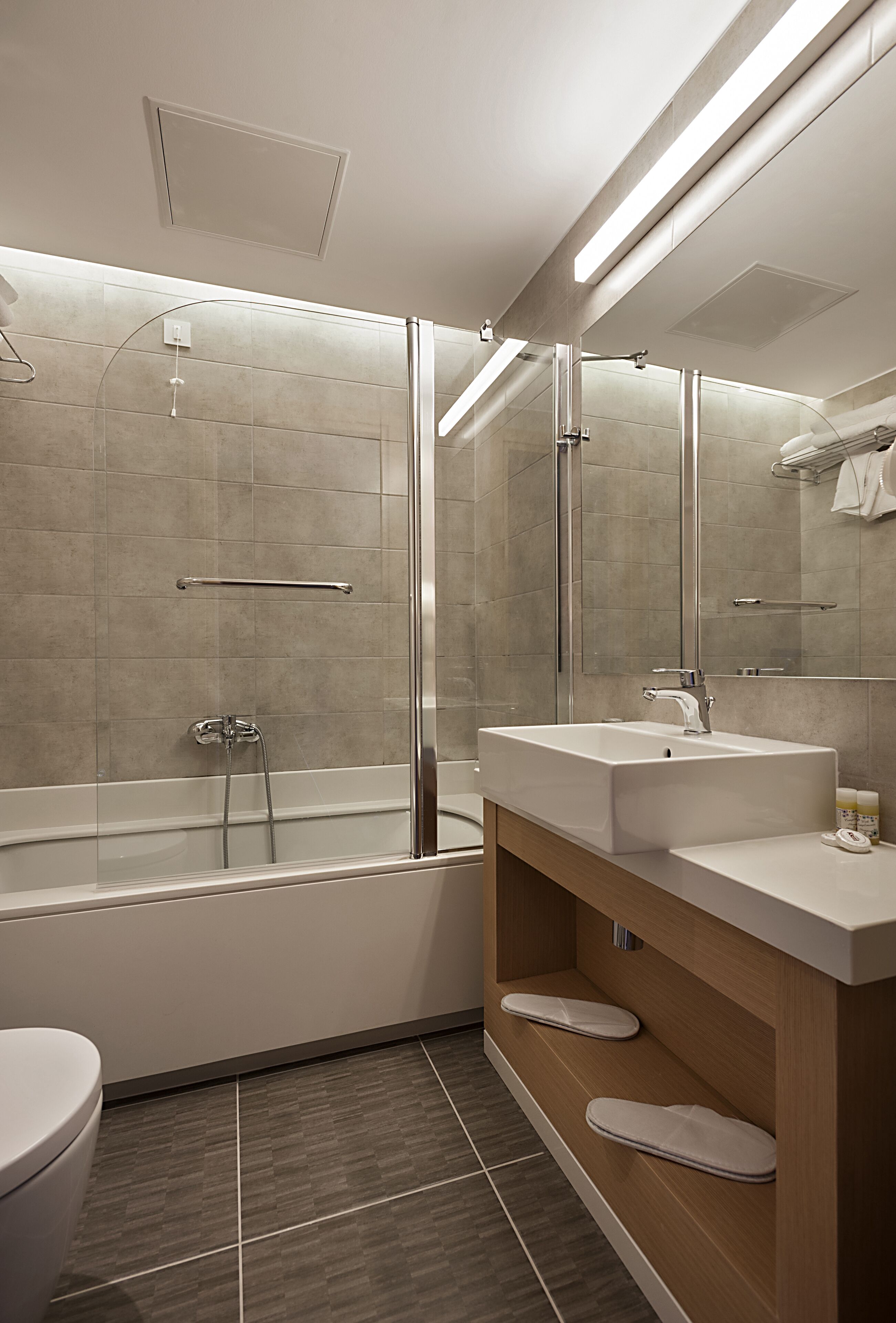 A modern bathroom with a glass-enclosed shower, a white sink, and a wooden vanity.