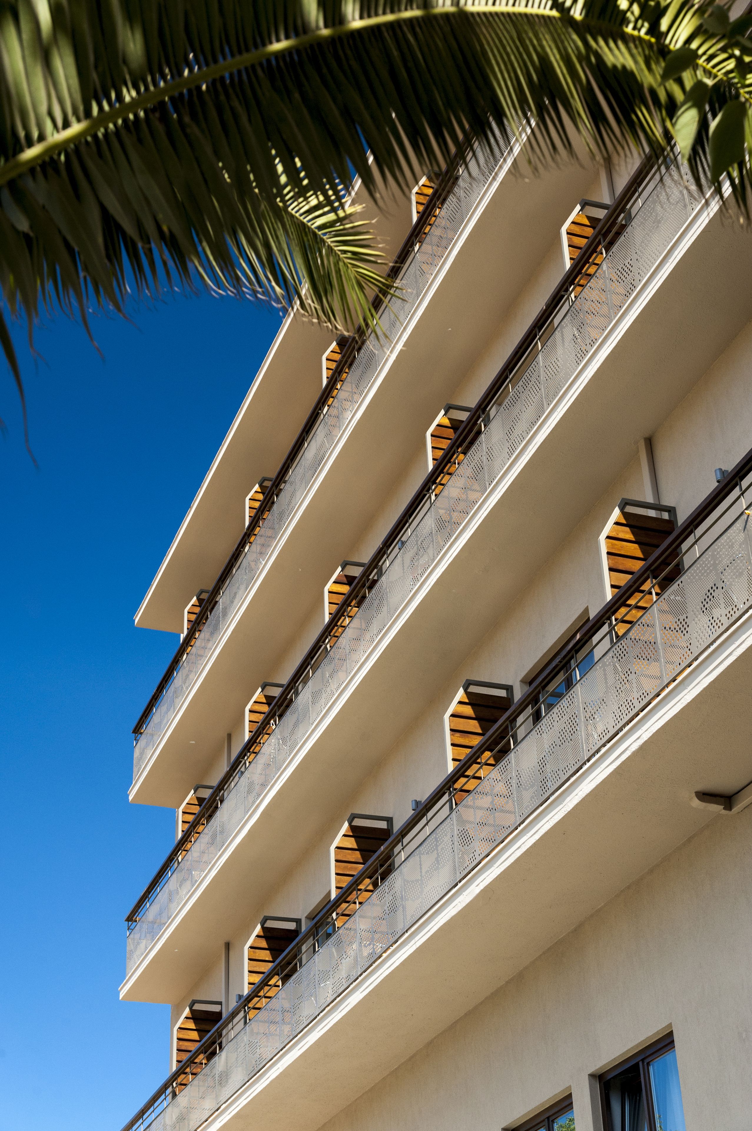A multi-story building with balconies, each with a metal railing and a small window.