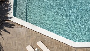Una piscina con agua cristalina, rodeada de suelo de baldosas y dos sillas de descanso.