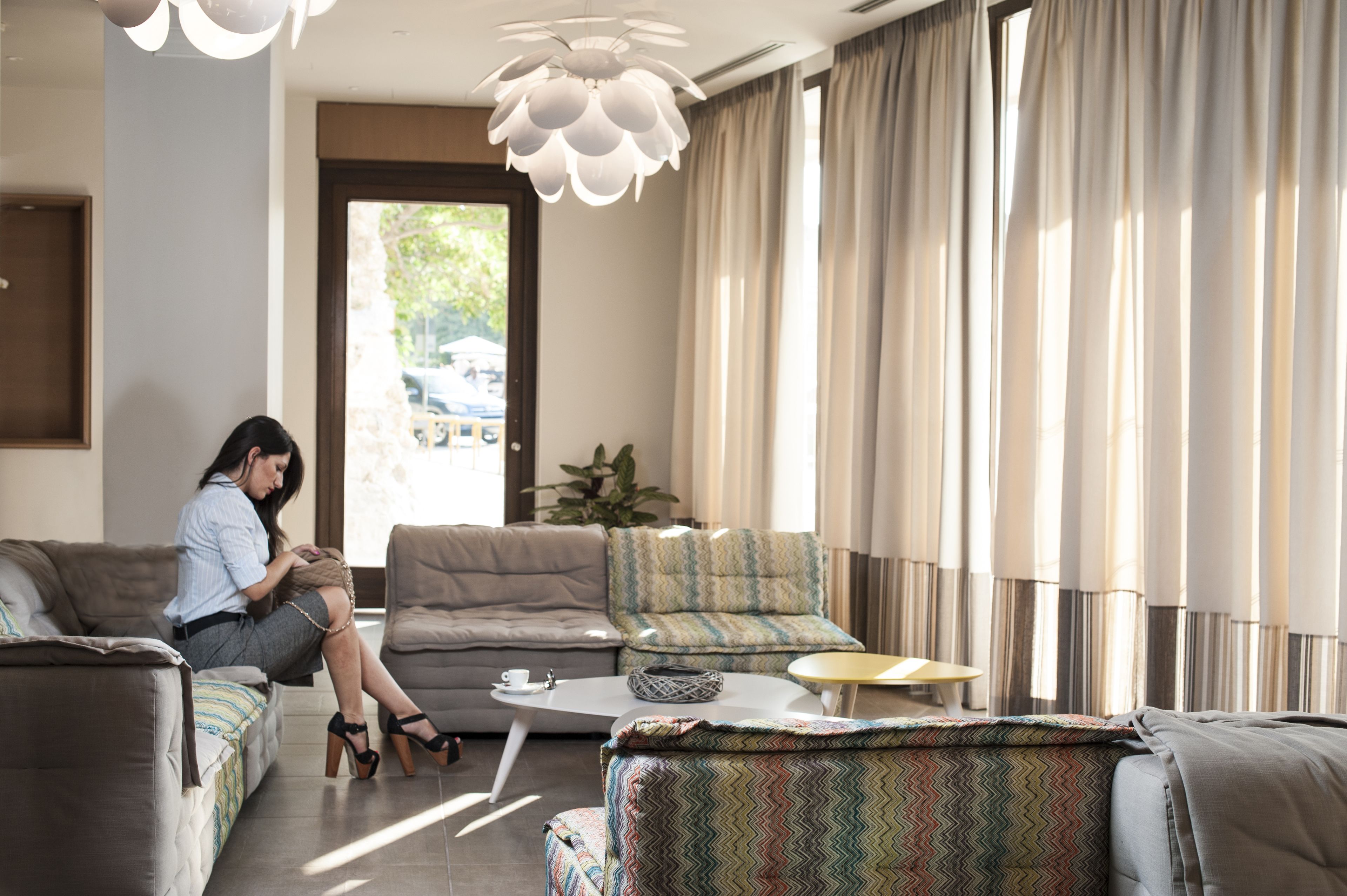 A modern living room with a sofa, armchair, and ottoman, a coffee table, and a large window with curtains.