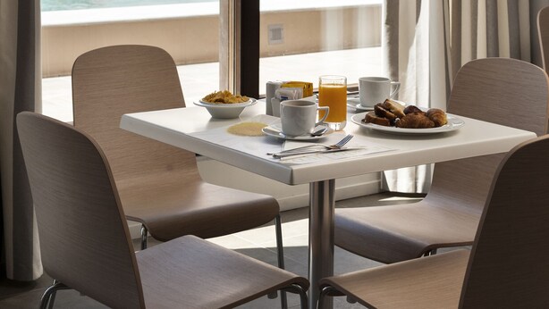 Habitación de hotel con comedor, vista a una piscina y una mesa lista para el desayuno.