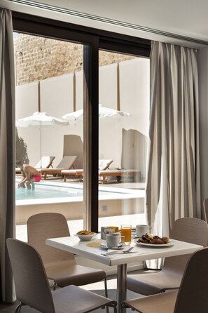 A hotel room with a dining area, a view of a pool, and a table set with breakfast. - Kriti Hotel (Chania)