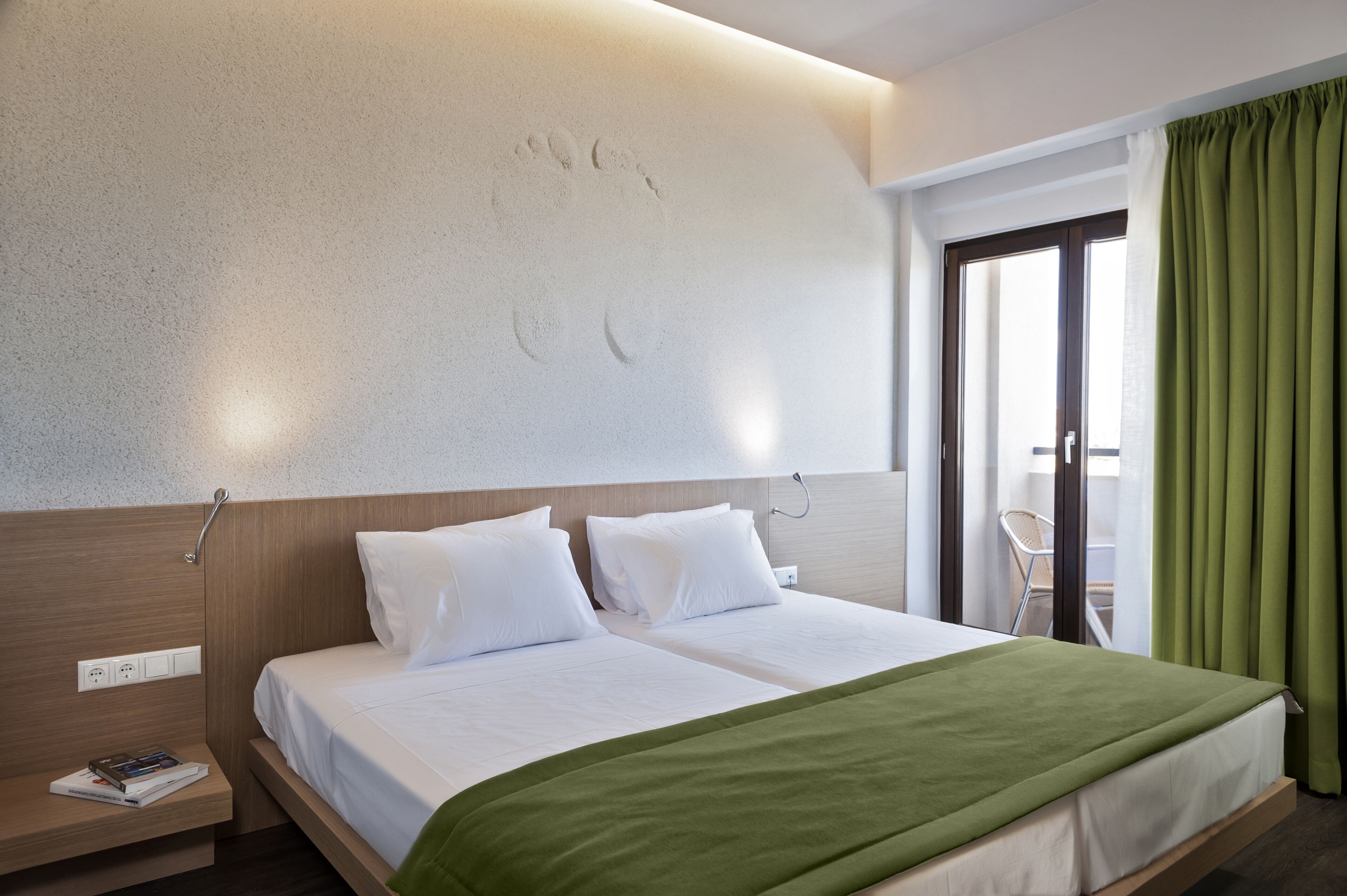Habitación de hotel con cama doble, mesita de noche con lámpara y ventana con cortinas.