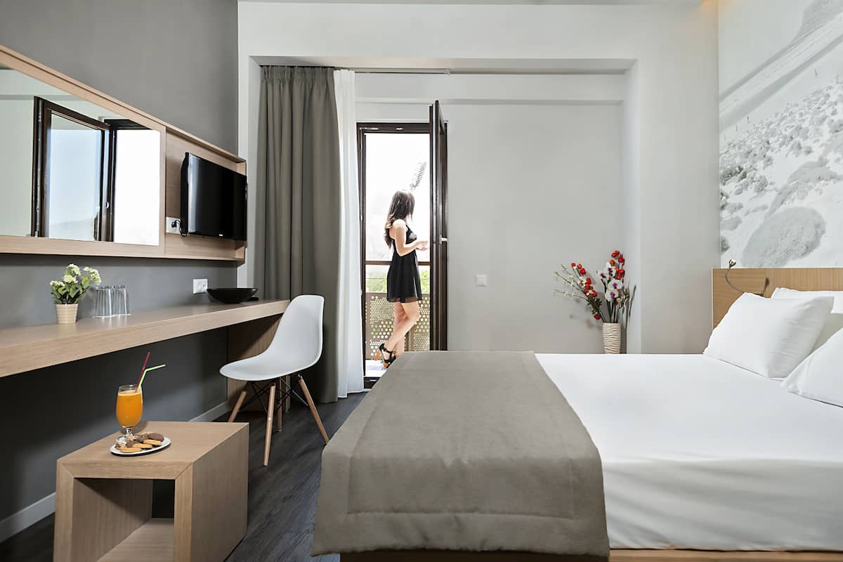 Una habitación de hotel con una cama, un escritorio, un televisor y una ventana con cortinas.