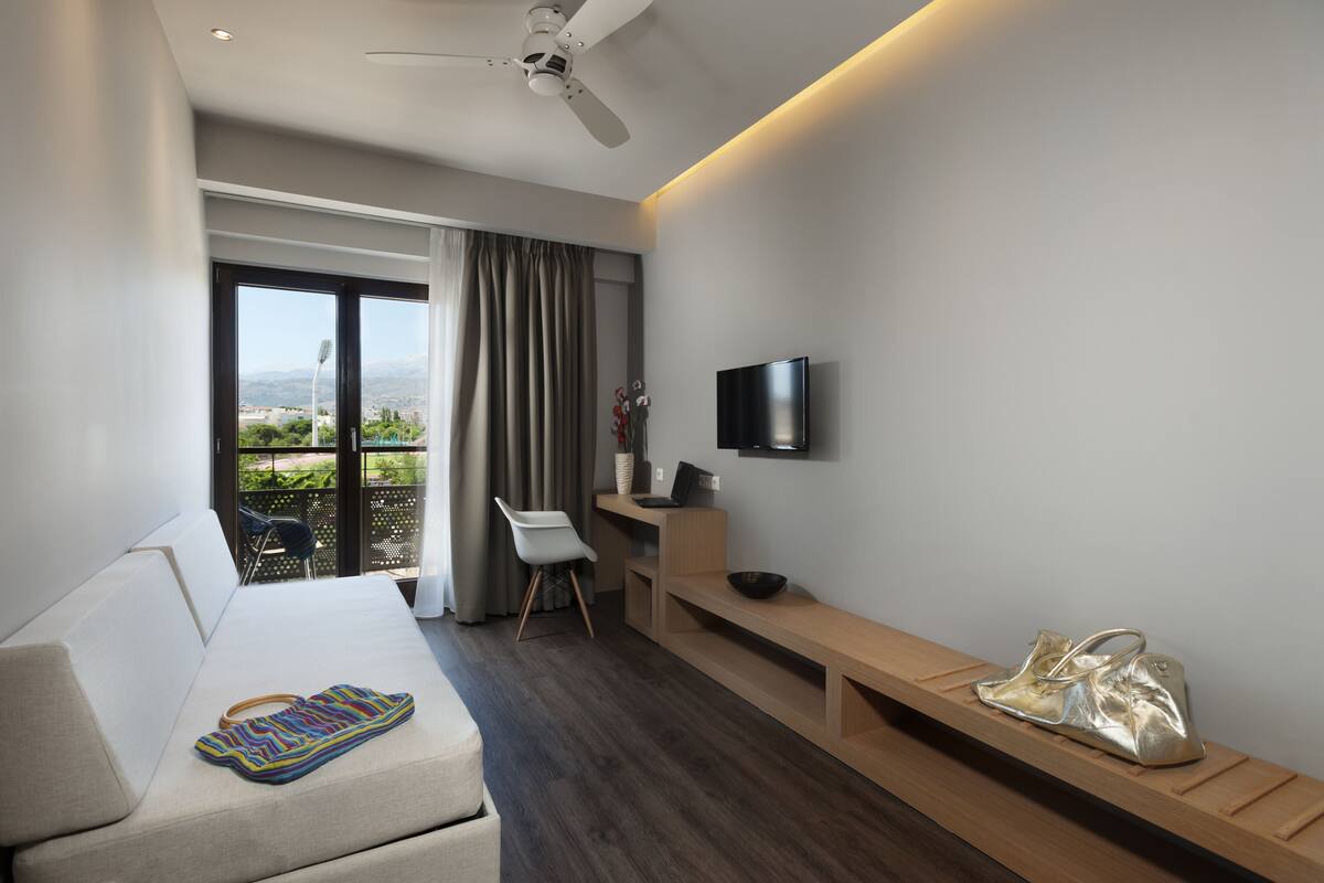 Una habitación de hotel moderna con sofá, escritorio, televisión y balcón con vistas.