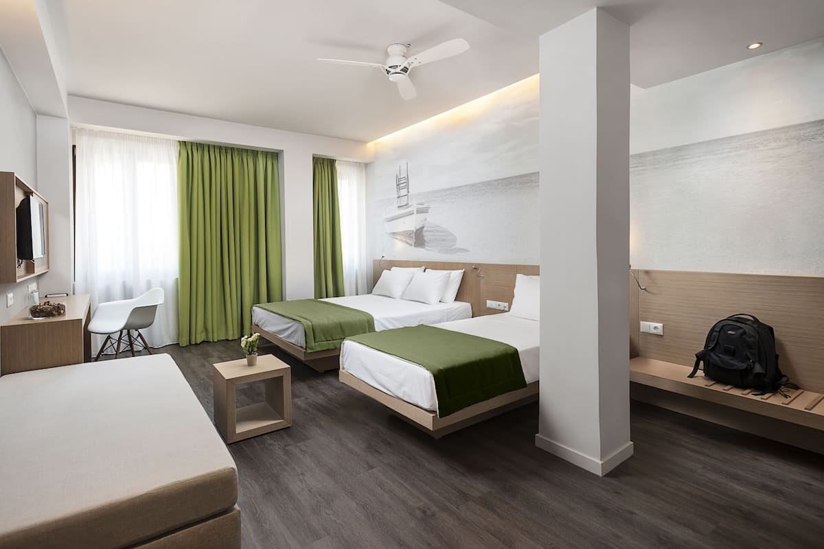 Habitación de hotel con dos camas, un escritorio, una silla, un televisor y un ventilador de techo.