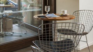 Una habitación moderna con puerta de vidrio, una pequeña mesa con sillas, un vaso de agua y una revista.