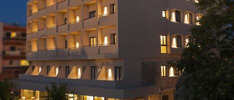 A multi-story hotel with a modern facade, multiple balconies, and a well-lit entrance.