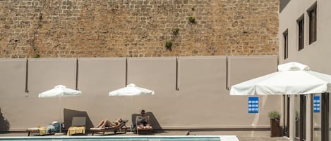 A pool area with lounge chairs, umbrellas, and a stone wall in the background.