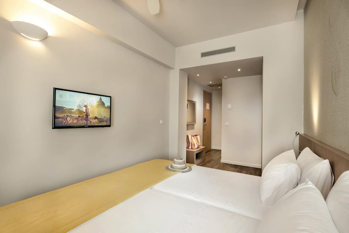 Habitación de hotel con cama, mesita de noche, televisión montada en la pared y puerta que da a otra habitación.