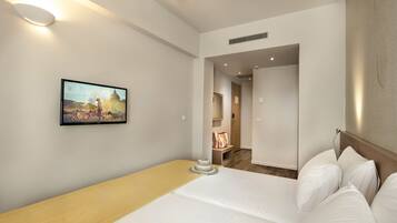 Habitación de hotel con cama, mesita de noche, televisión montada en la pared y puerta que da a otra habitación.