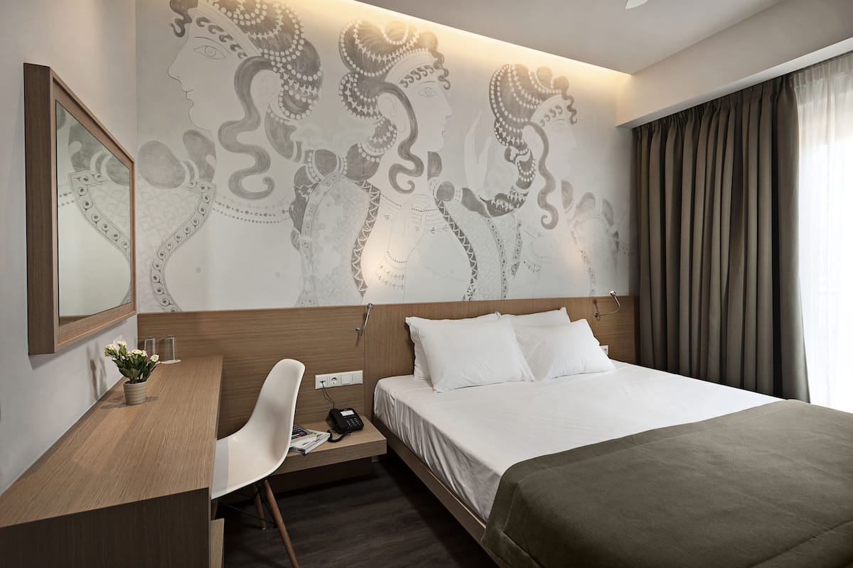 Habitación de hotel con una cama, un escritorio, una silla, un teléfono y una pared con un mural decorativo.