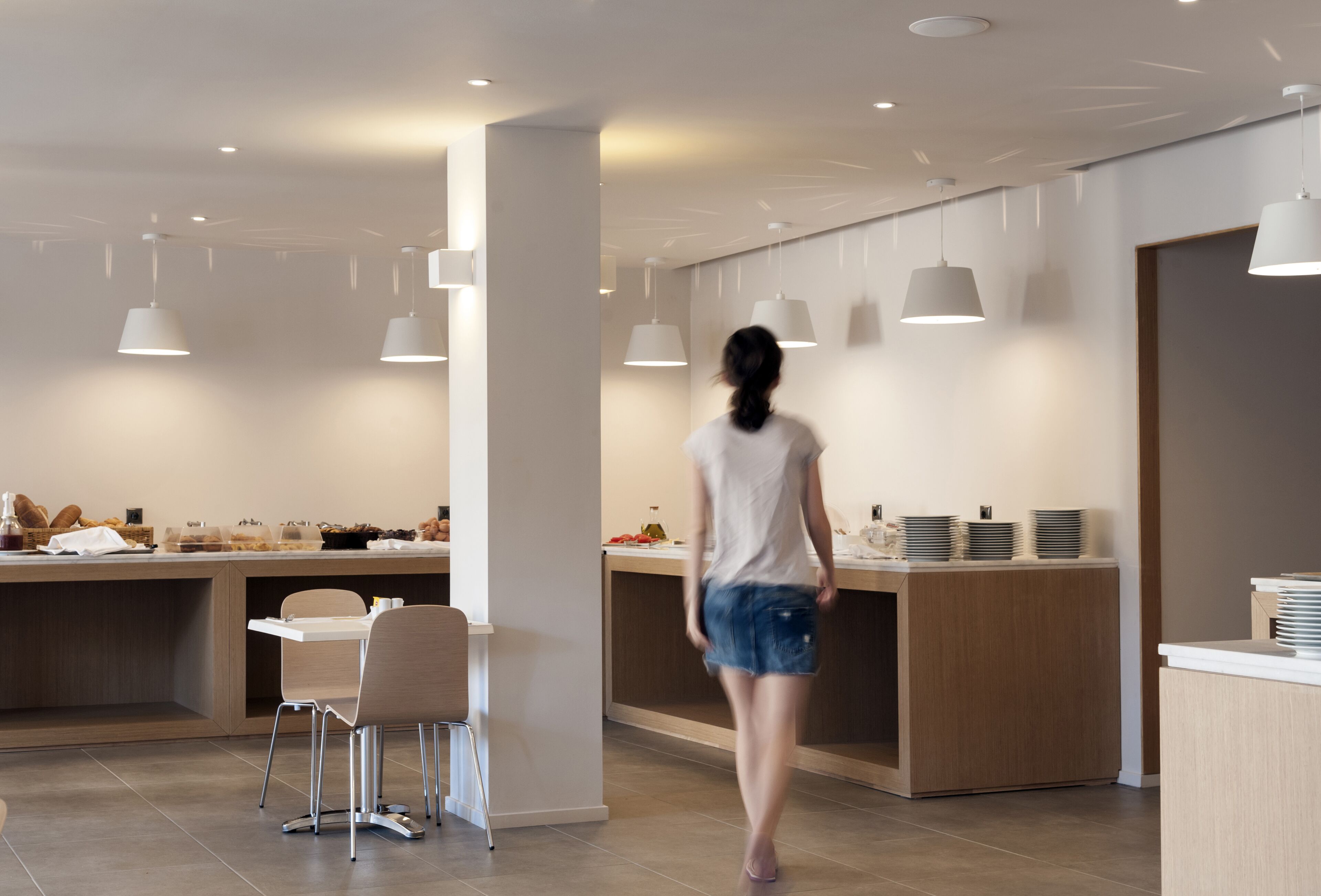A modern kitchen with a central island, pendant lighting, and a person walking towards the island.